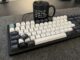 Mechanische Tastatur mit schwarz-weißen Tastenkappen auf einer grauen Filzunterlage. Unten links sitzt eine dunkle Taste mit Tux-Logo anstelle der Windows-Taste. Eine abgezogene schwarze Kappe mit Windows-Logo liegt lose auf den Tasten. Dahinter steht eine schwarze Tasse mit der Aufschrift: "I'm from IT. Please step now away from the keyboard!"
